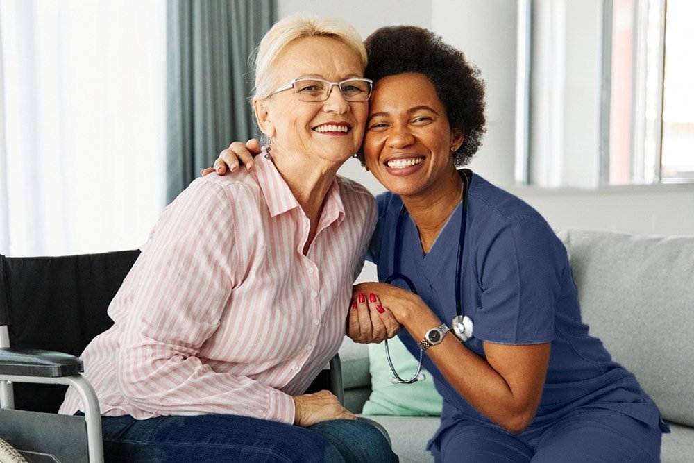 Private duty nurse in navy scrubs hugging an older woman at home